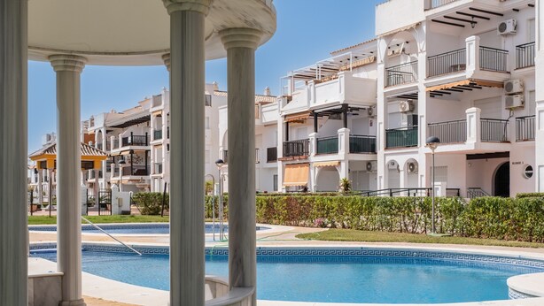 A pool area with a clear view of a building with multiple balconies and a well-maintained lawn. - Apartment 'Beachfront Apt Torrox Costa' with Sea View, Wi-Fi and Air Conditioning (Torrox)