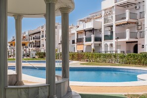 Zona de piscina con vista despejada a un edificio con múltiples balcones y un césped cuidado.