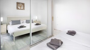 A hotel room with a bed, a bedside table, a nightstand, a mirror, and a wall art piece. - Apartment 'Beachfront Apt Torrox Costa' with Sea View, Wi-Fi and Air Conditioning (Torrox)