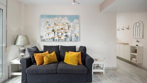 A modern living room with a grey sofa, a painting of a coastal village, and a minimalist decor style. - Apartment 'Beachfront Apt Torrox Costa' with Sea View, Wi-Fi and Air Conditioning (Torrox)