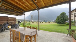 A covered outdoor seating area with a table and chairs, a scooter, and a view of a farm with cows. - Private room with mountain view, shared terrace and Wi-Fi (Pont-Saint-Martin)