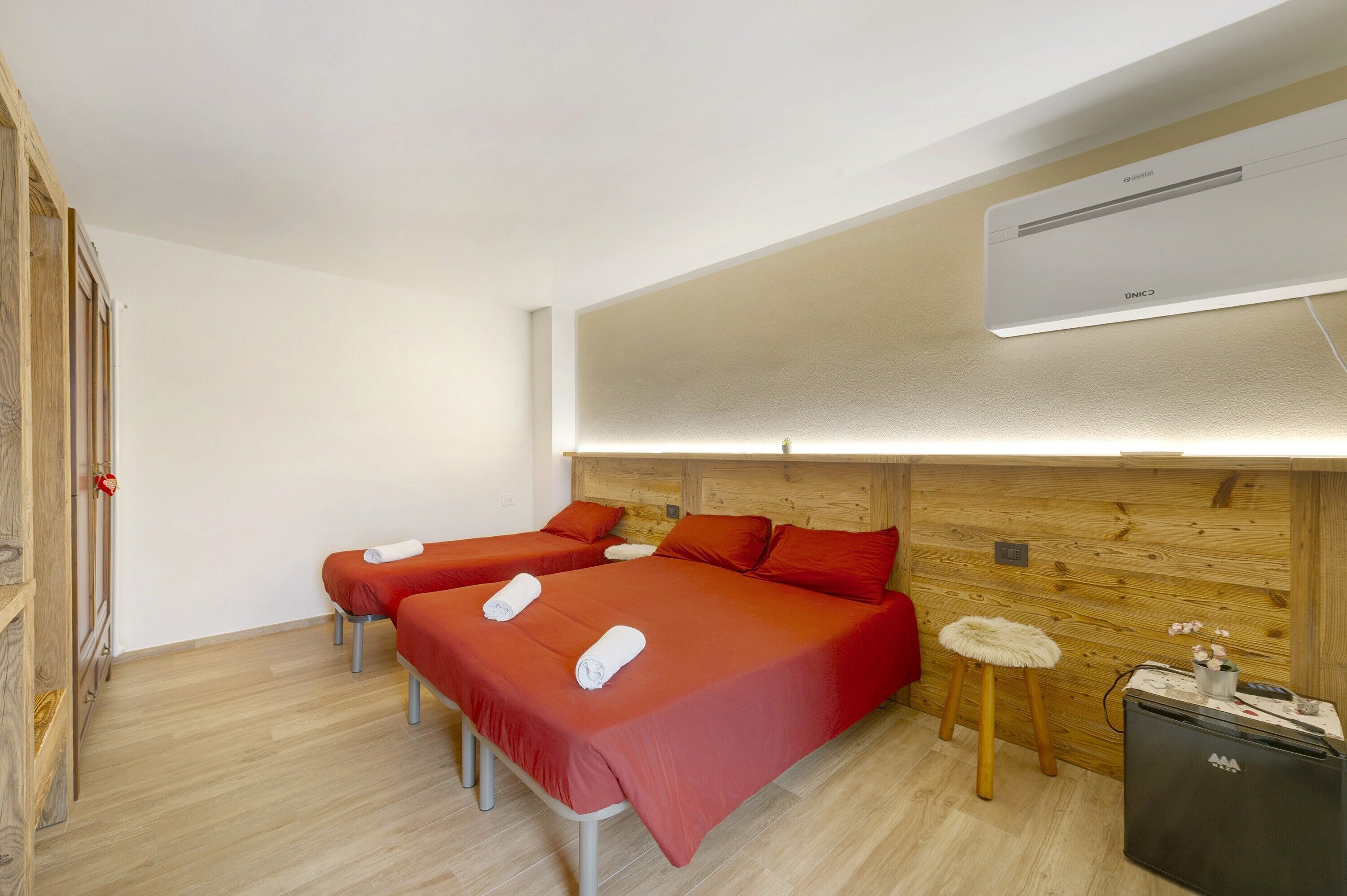 Ein Hotelzimmer mit zwei Betten, einem Holzkopfende, einem kleinen Hocker, einem Kühlschrank und einer Klimaanlage.