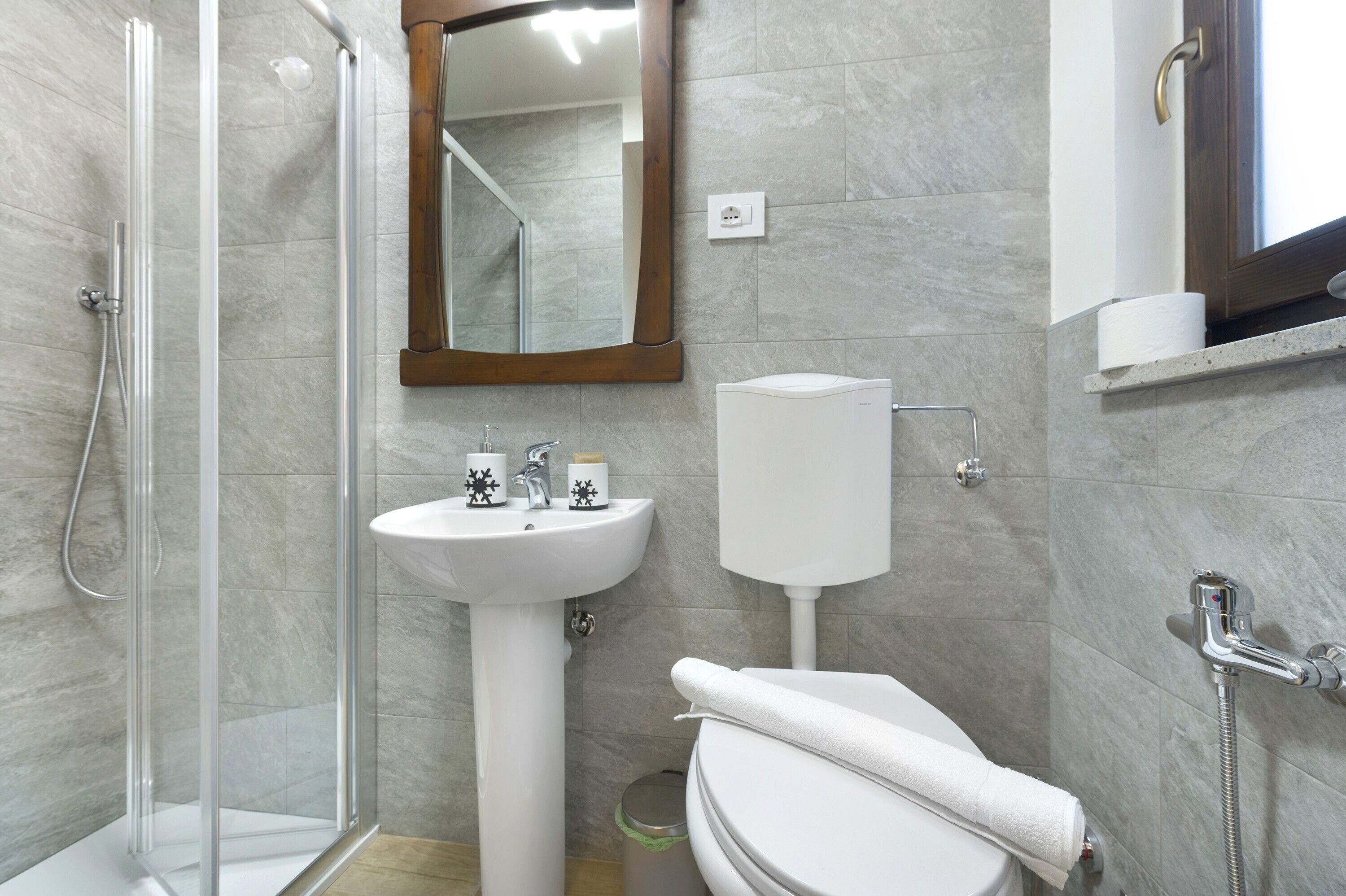 A bathroom with a glass shower enclosure, a pedestal sink, a toilet, and a mirror.