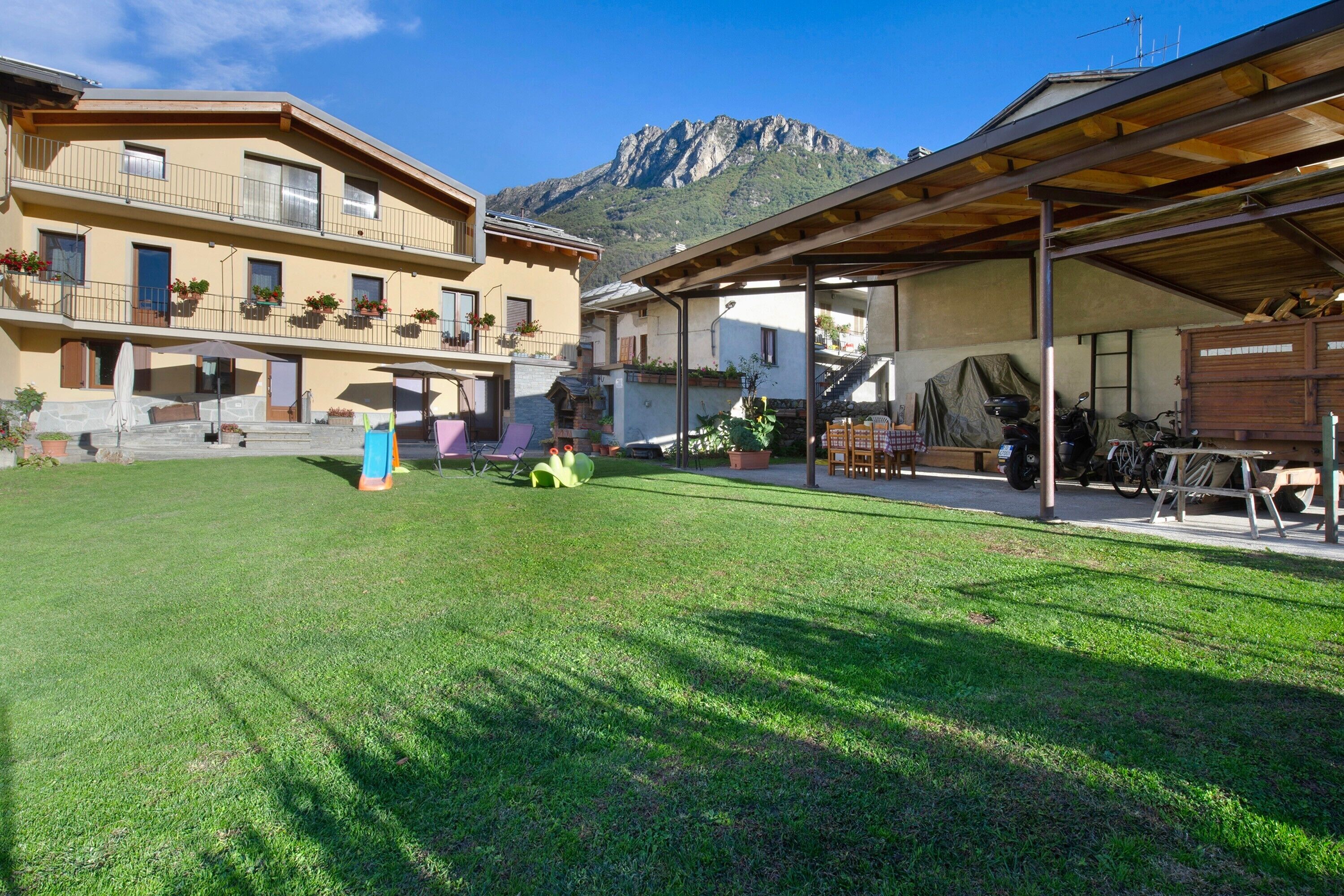 A courtyard with a mountain backdrop, outdoor seating, and a covered area with a motorcycle.