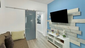 Una sala de estar moderna con un sofá, un televisor montado en una pared de madera, un puerta corredera y una consola blanca.