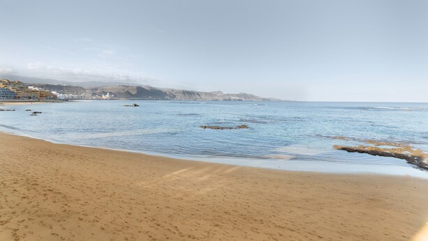 Una playa con aguas cristalinas, una orilla arenosa y montañas a lo lejos.