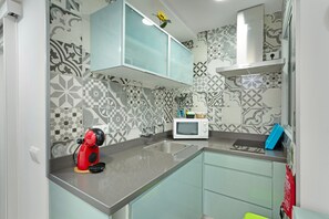 A kitchen with patterned tiles, a microwave, a red coffee maker, and a blue container on the counter.