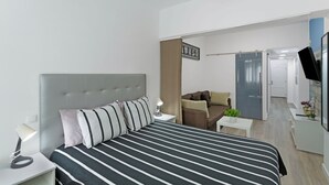 Una habitación de hotel moderna con cama, lámpara de noche, una mesita con una planta y televisor sobre un mueble.
