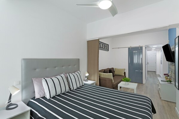 A modern hotel room with a bed, bedside lamp, a small table with a plant, and a TV on a stand.