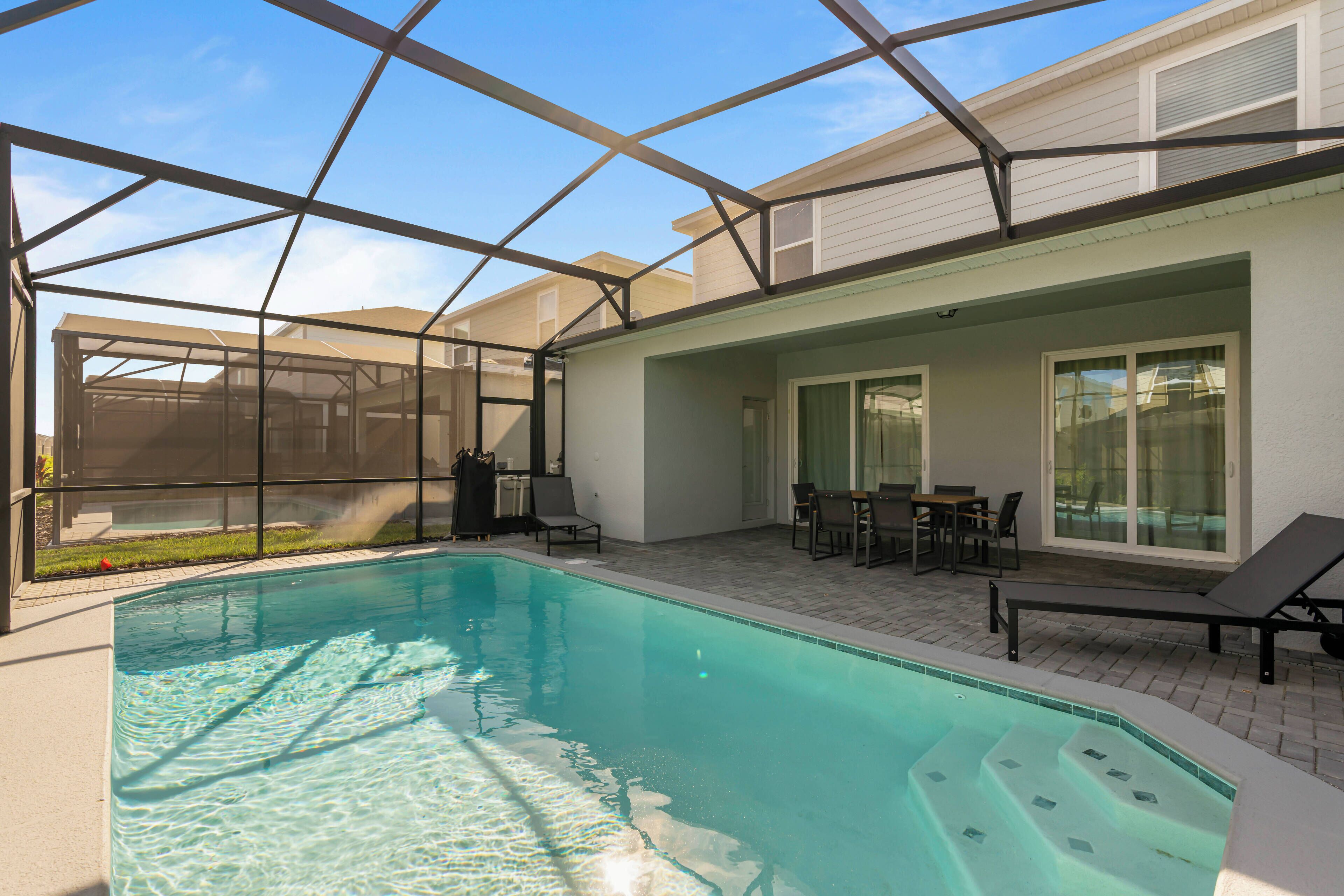 A swimming pool with a glass enclosure, a patio area with outdoor furniture, and a view of the backyard.