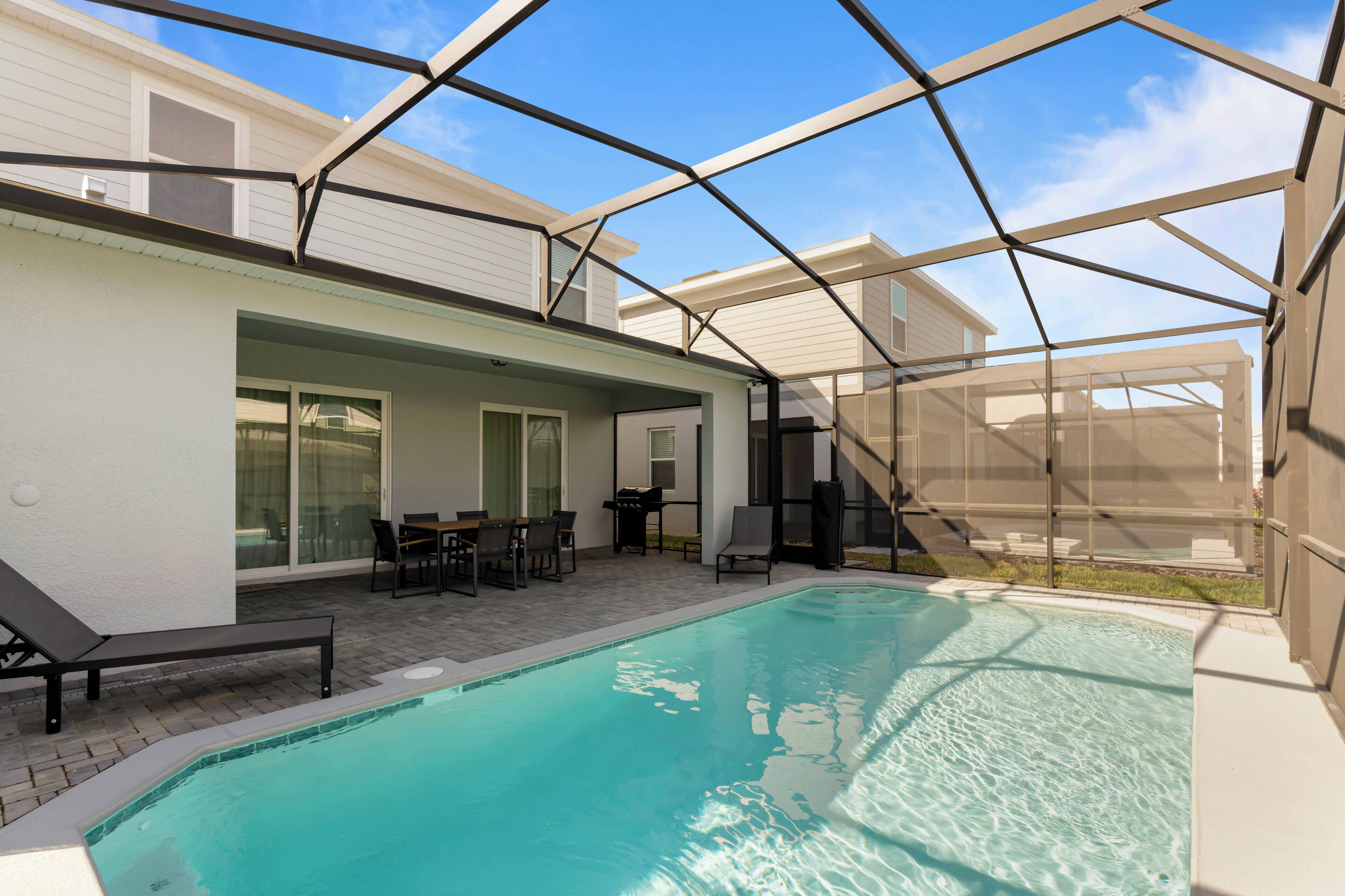 An outdoor swimming pool with a covered patio area, a table, and chairs.