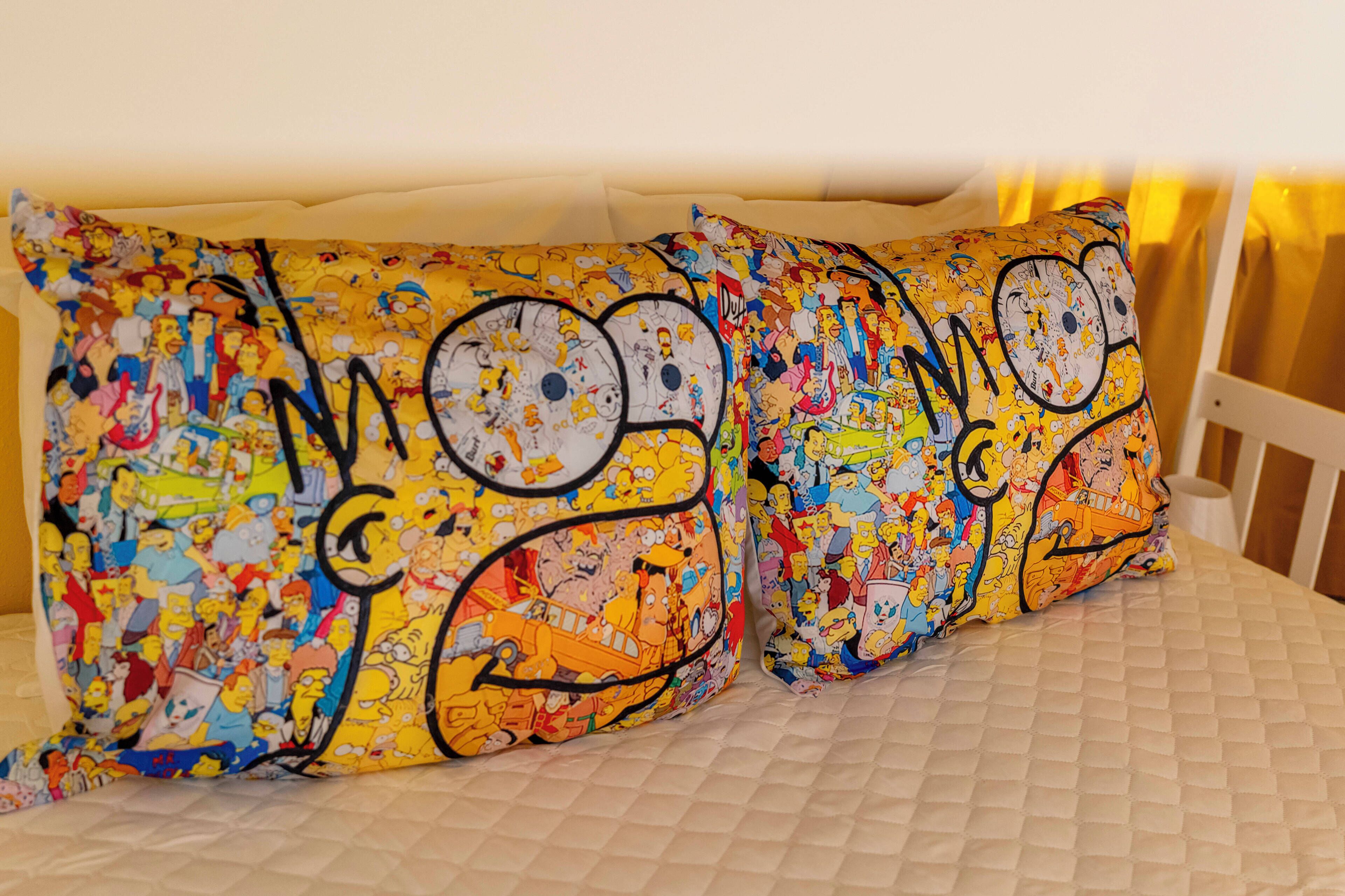 A bed with a quilted white mattress and pillows featuring a colorful cartoon character print.