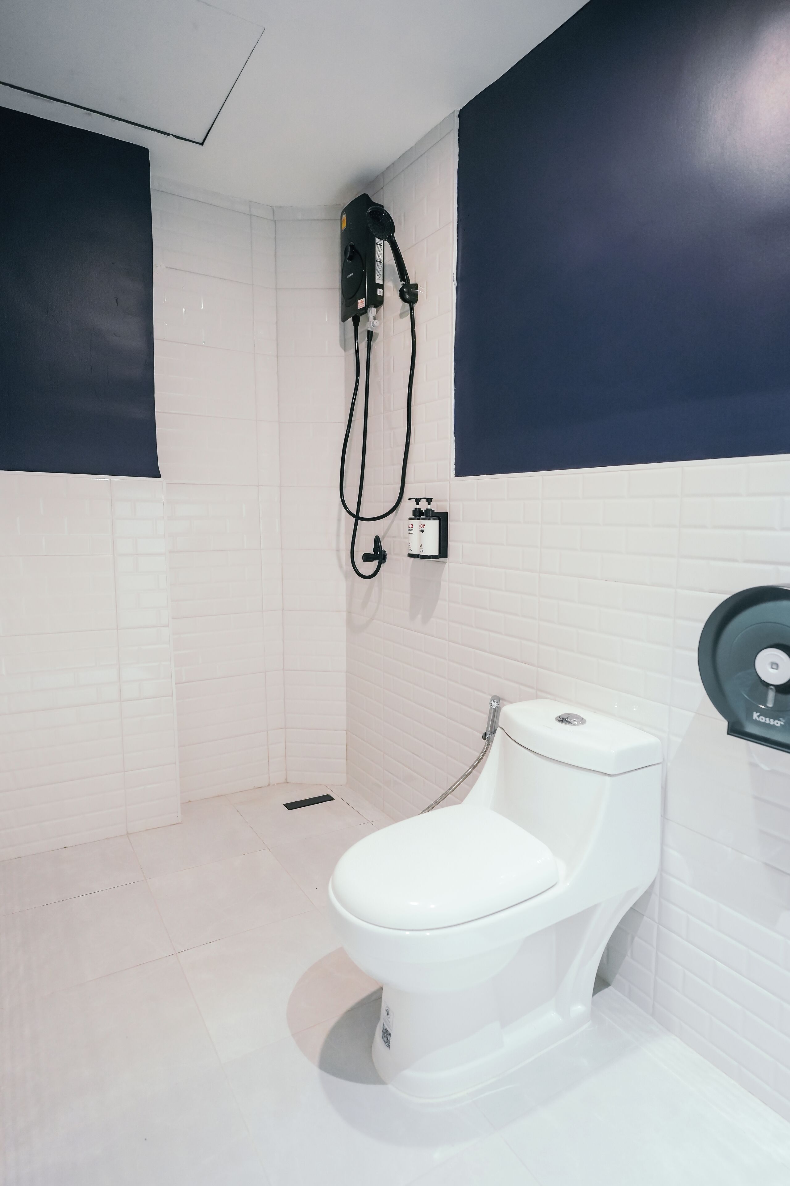Un bagno moderno con pareti piastrellate in bianco, un WC bianco e una doccia con pannello di controllo nero.