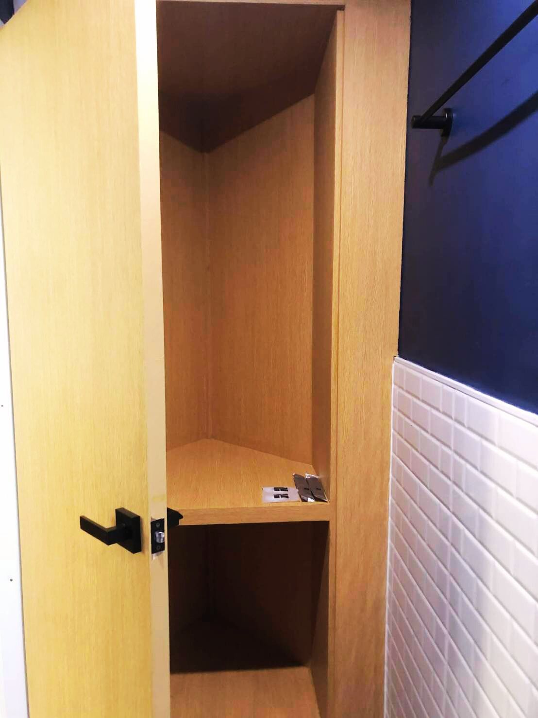 A wooden cabinet with a black handle, a white tiled wall, and a blue wall in the background.