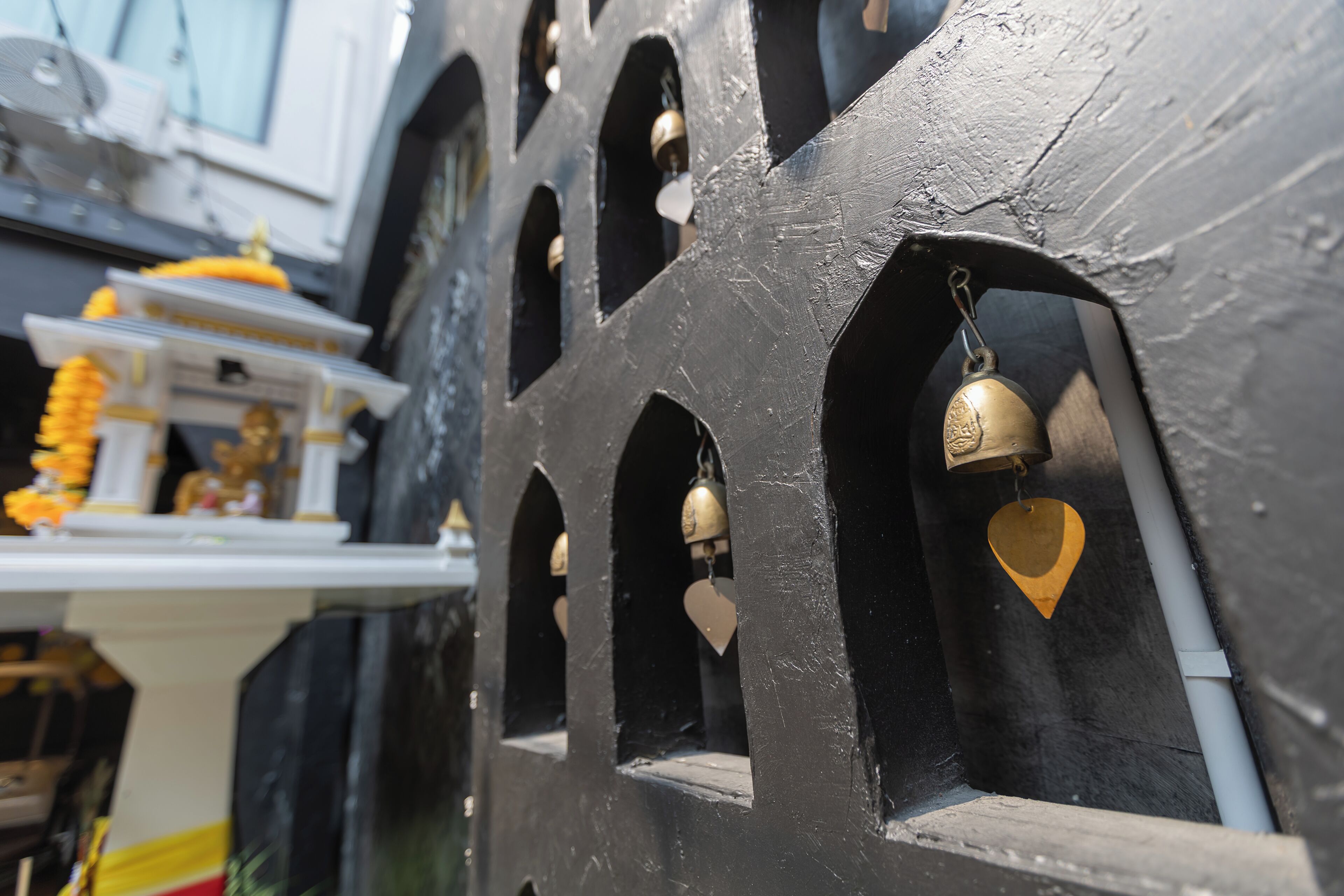 A close-up of a black structure with multiple arched openings, some with bells inside.