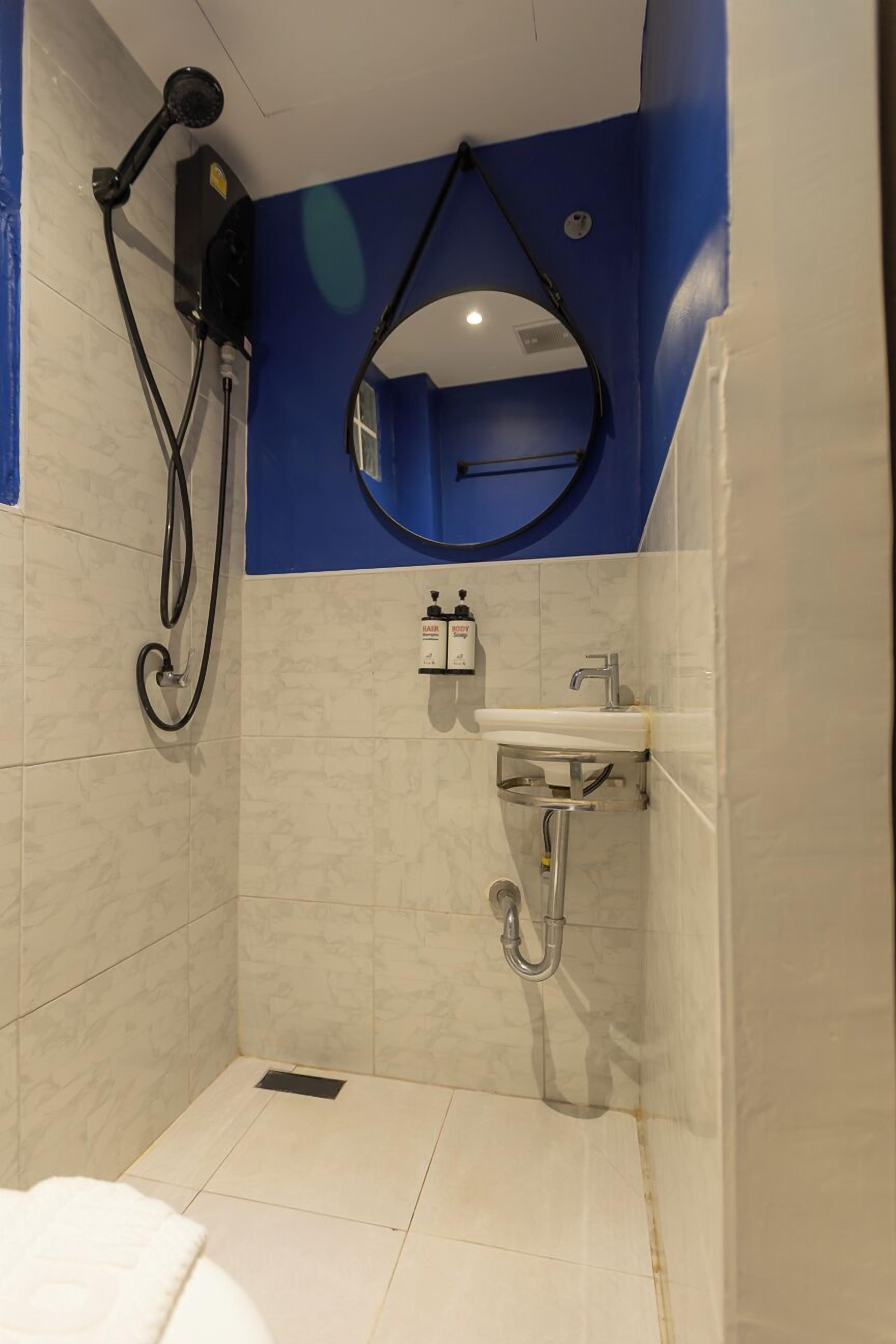 A small, enclosed shower area with a handheld showerhead, a wall-mounted mirror, and a sink with a faucet.