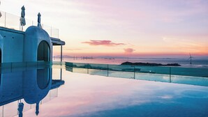 A modern building with a glass balcony overlooking a calm body of water and a sunset sky. - YOOOO SEA TRUE REST HOTEL (Fuzhou)