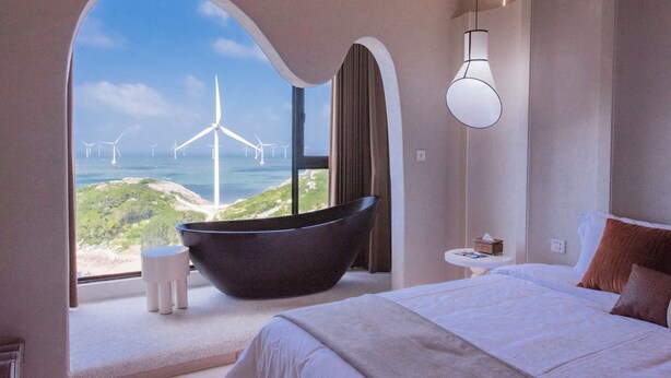 A modern hotel room with a large window offering a view of wind turbines and a coastal landscape. - YOOOO SEA TRUE REST HOTEL (Fuzhou)