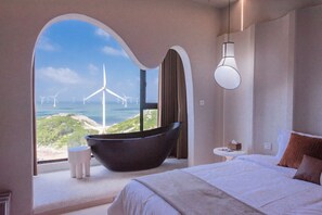 A modern hotel room with a large window offering a view of wind turbines and a coastal landscape.