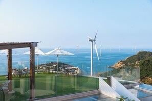 A rooftop terrace with outdoor seating, overlooking a coastal area with wind turbines and the sea.