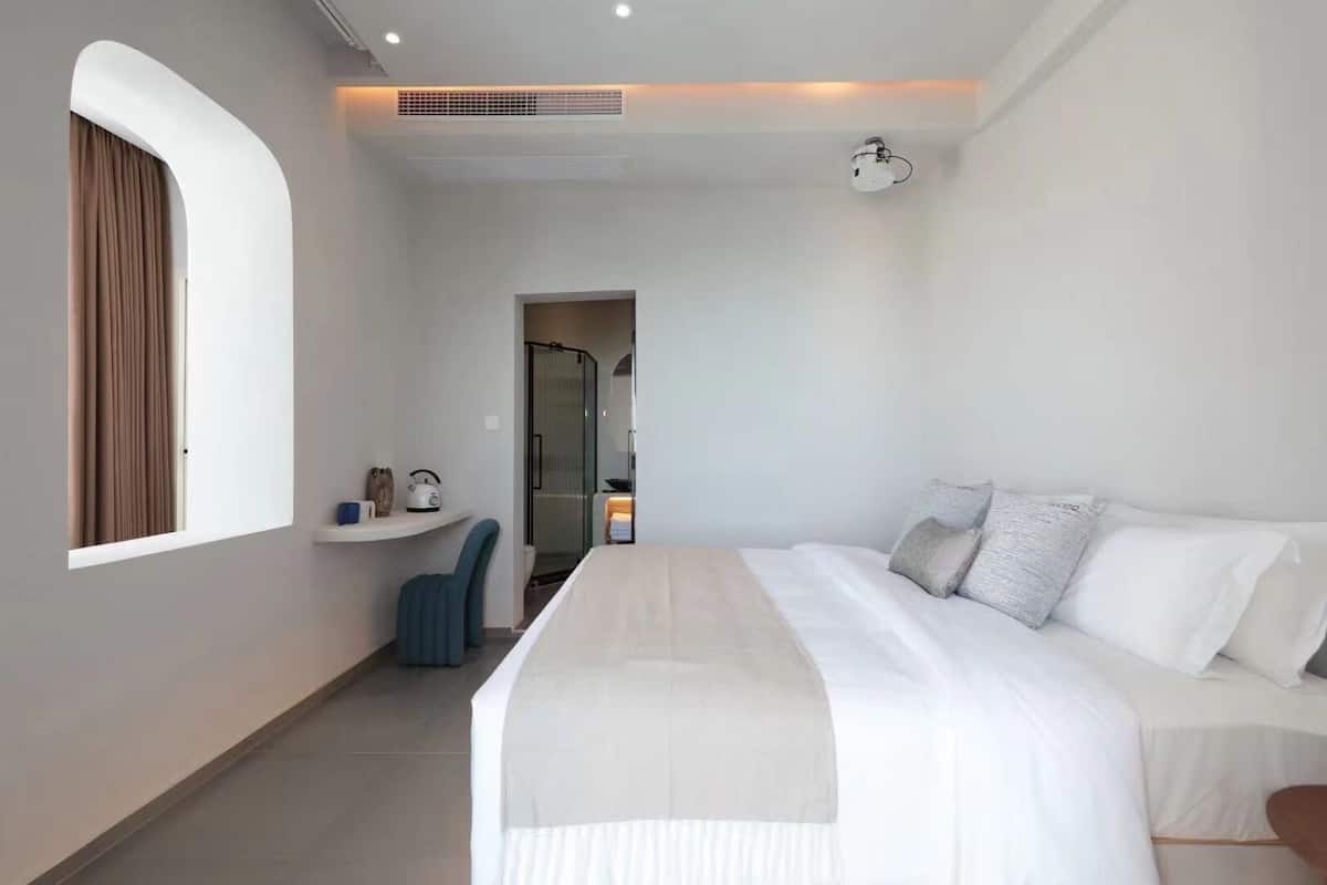 A modern hotel room with a large bed, a desk with a chair, and a shower area.
