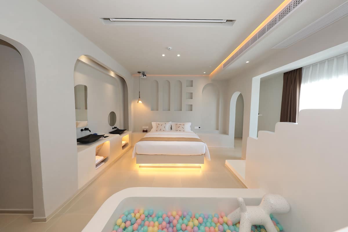 A modern bedroom with a large bed, a vanity, and a bathtub filled with colorful balls.
