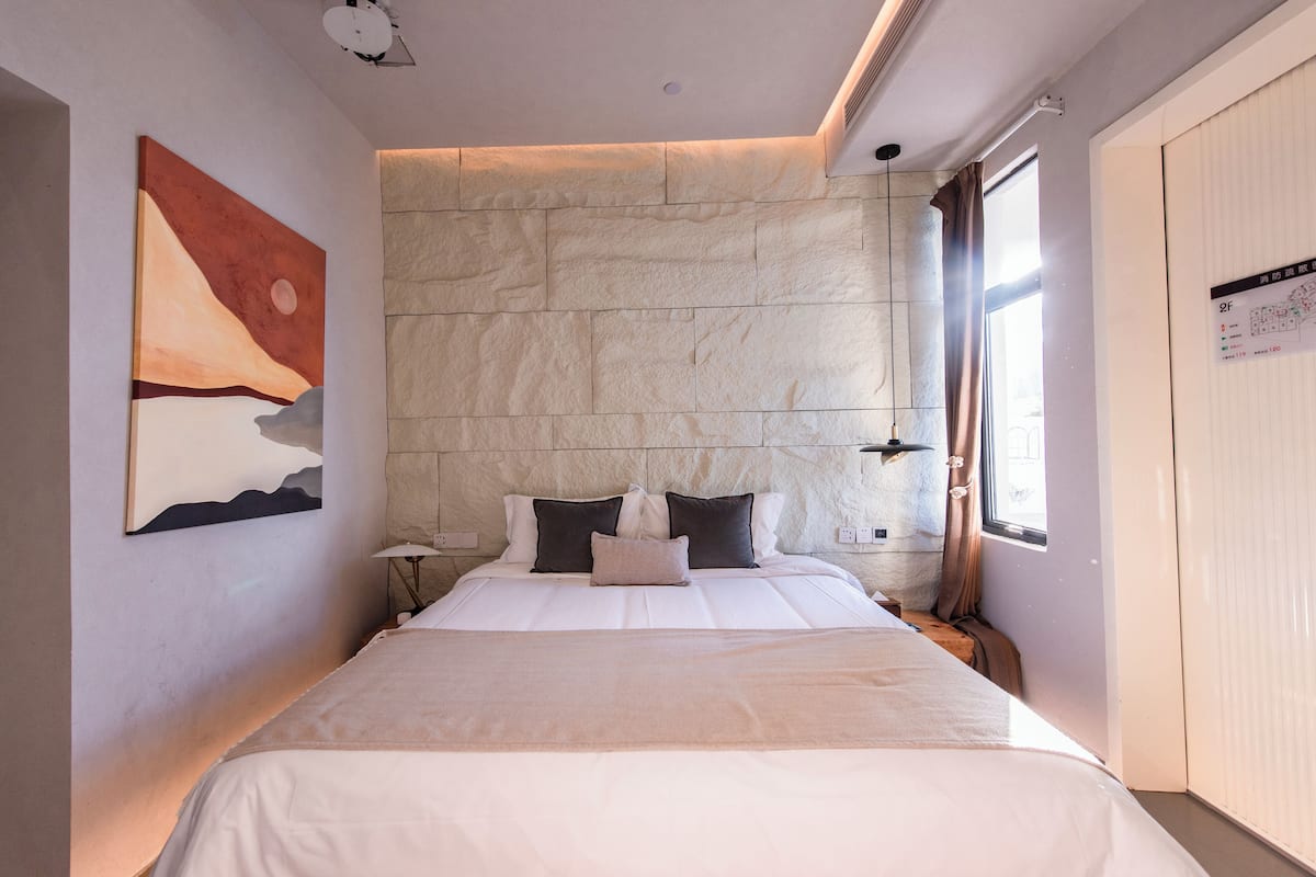 A modern hotel room with a large bed, stone wall, and a painting on the wall.