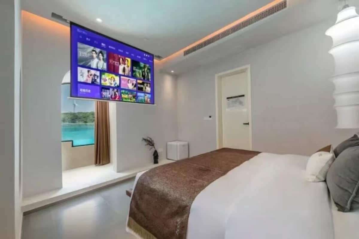 A modern hotel room with a large bed, a flat-screen TV mounted on the wall, and a view of a swimming pool.
