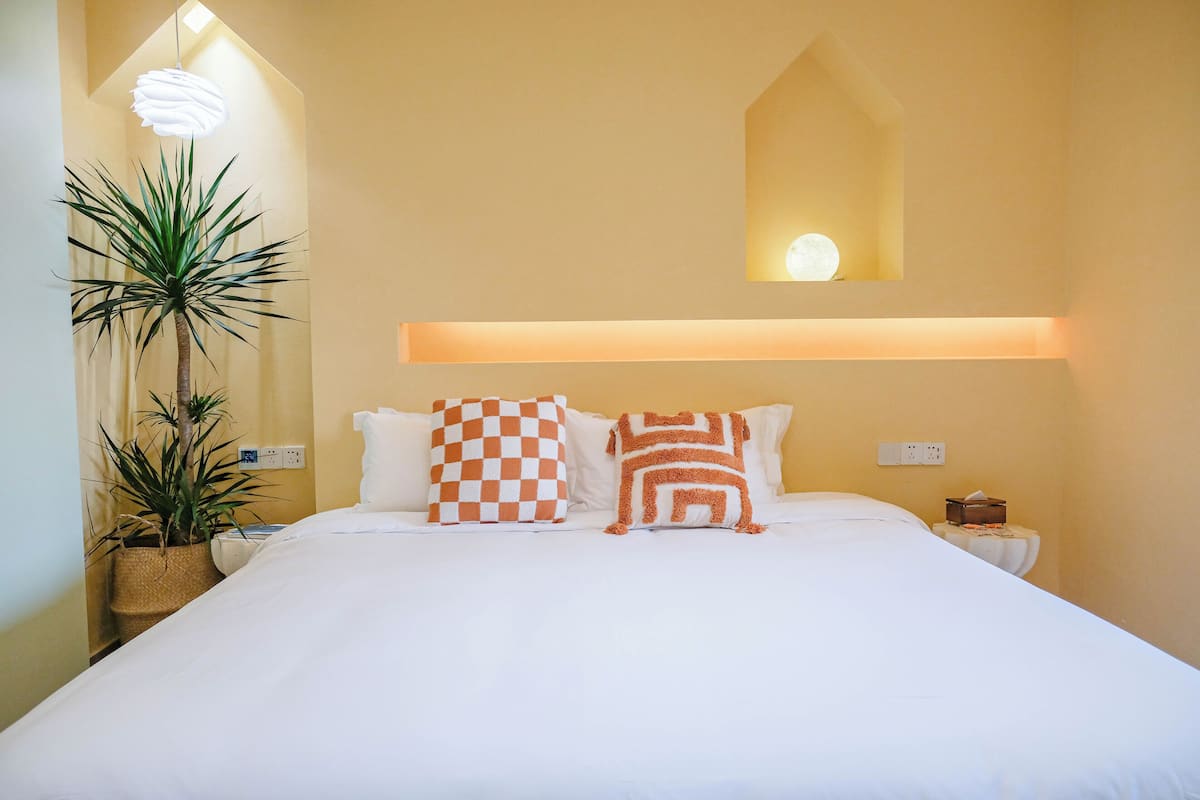 A neatly made bed with two pillows, a bedside table with a tissue box, and a wall-mounted light fixture.
