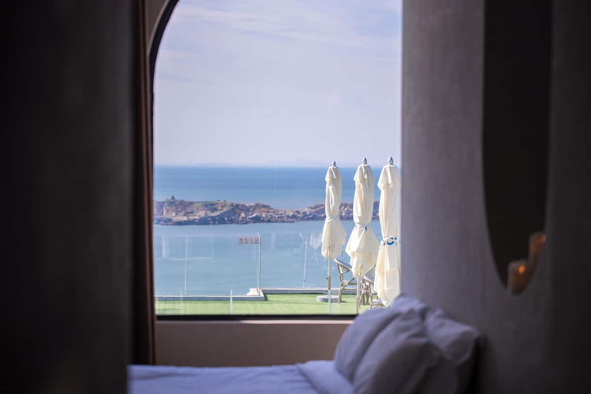 A room with a large window overlooking a beach with umbrellas and a sign.