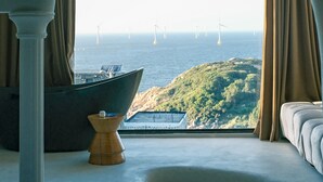 A room with a large window overlooking a coastal area with wind turbines, a boat, and a hillside. - YOOOO SEA TRUE REST HOTEL (Fuzhou)