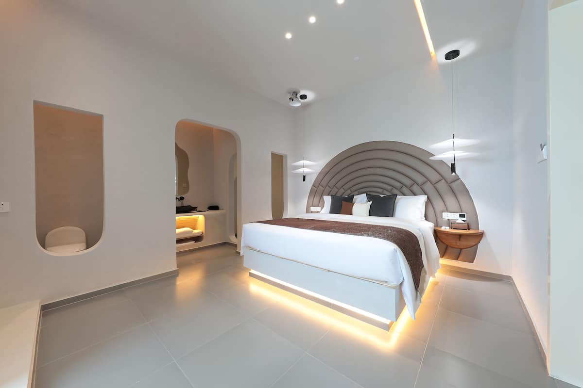 A modern bedroom with a large bed, a curved wall design, and integrated lighting.
