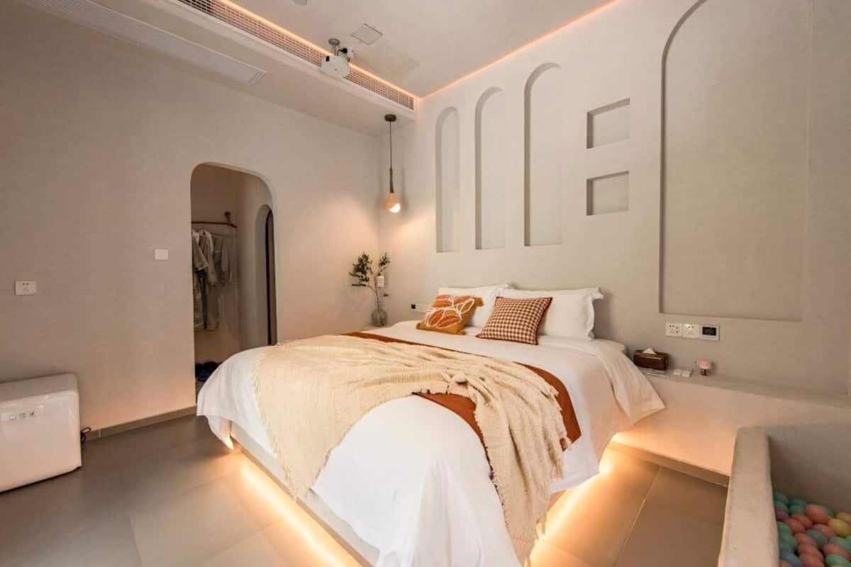 A modern bedroom with a large bed, a bedside table, a mirror, and a wall-mounted light fixture.