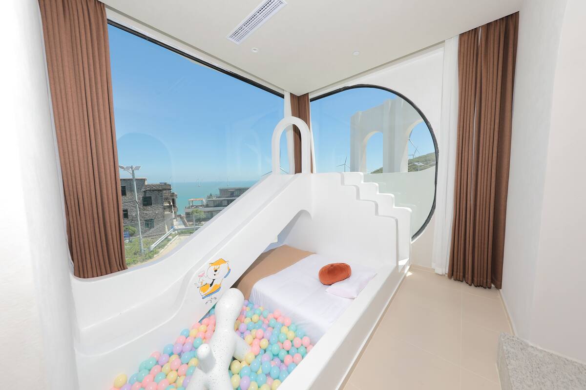 A child’s play area with a slide, colorful balls, and a view of the city.