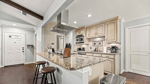 Una cocina moderna con una isla de granito, taburetes de bar, electrodomésticos de acero inoxidable y armarios de madera.