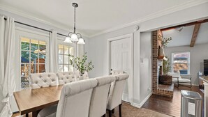 Un comedor con una mesa de madera y sillas acolchadas, una lámpara colgante y vistas al exterior a través de amplios ventanales.