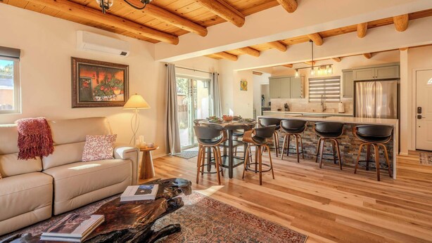 Un vaste espace de vie doté d’un plafond en bois, d’un canapé, d’une table basse et d’un coin repas avec des tabourets de bar.