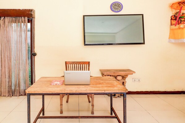 A room with a wooden table, a chair, a laptop, a television on the wall, and a curtain. - Collection O Putri Inn Homestay (Denpasar)