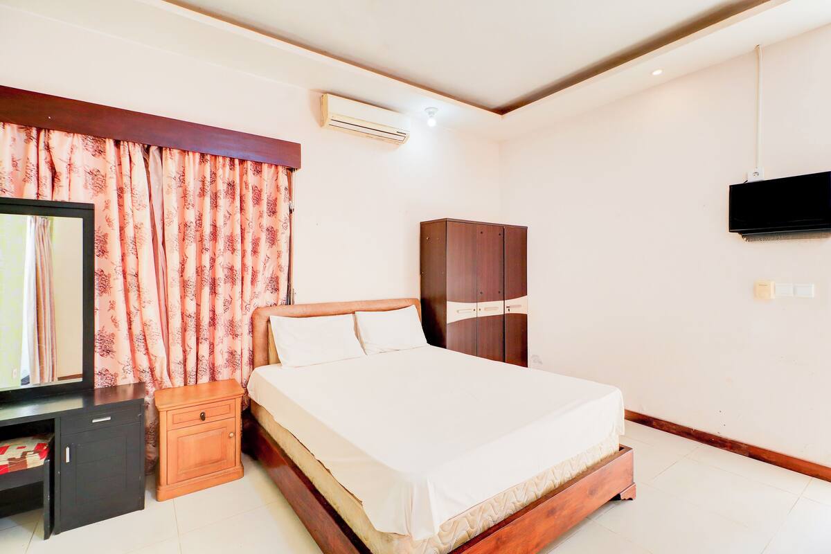 A bedroom with a bed, a wardrobe, a TV, a desk, and an air conditioning unit.