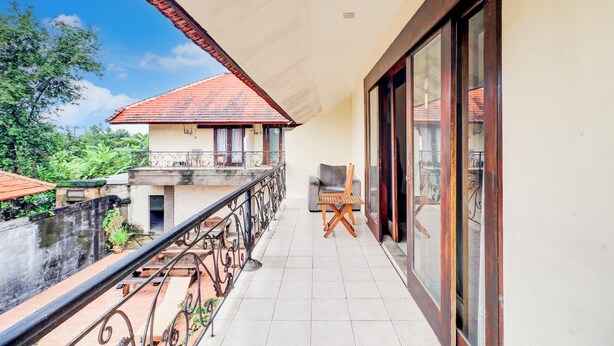 A balcony with a view of a house, a chair, and a table. - Collection O Putri Inn Homestay (Denpasar)