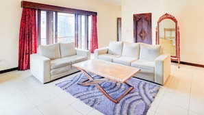 A living room with two white sofas, a wooden coffee table, and a blue patterned rug. - Collection O Putri Inn Homestay (Denpasar)