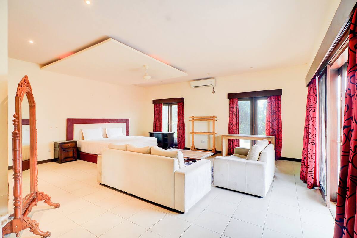 A hotel room with a bed, two sofas, a wooden dresser, a mirror, and a TV.