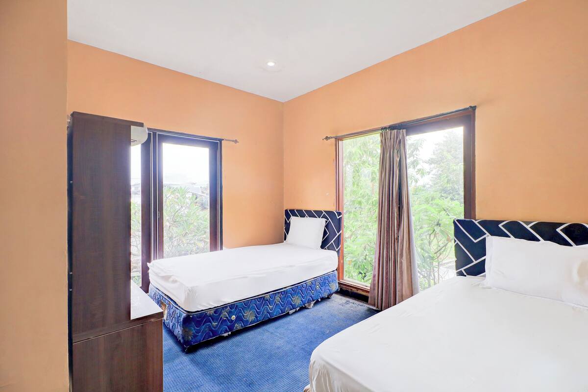 A hotel room with two beds, a large window with curtains, and a view of greenery outside.