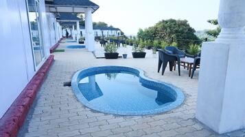 Un área de piscina con suelo de baldosas, mobiliario exterior y plantas en macetas.