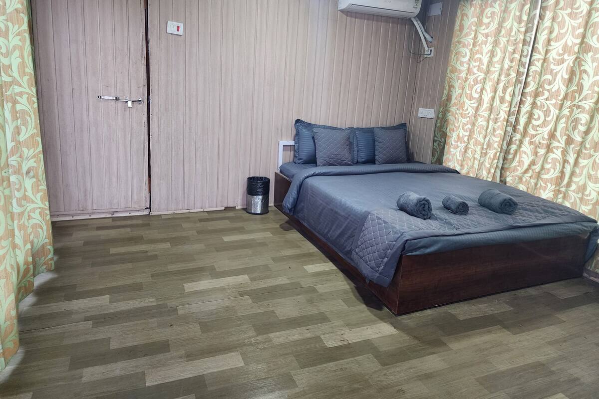 A bedroom with a bed, a wall-mounted air conditioner, a trash bin, and a door.