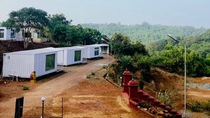 Una hilera de casas móviles blancas con un sendero de tierra que las conecta, rodeadas de vegetación y colinas al fondo.