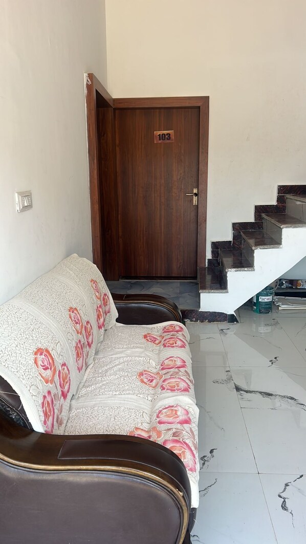 Une pièce avec un canapé, une porte en bois portant une plaque avec un numéro, et un escalier.
