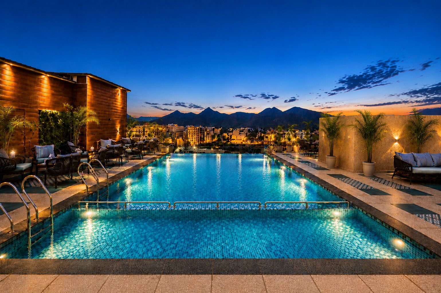 Una piscina con vista sulle montagne, lettini e un edificio con illuminazione calda.