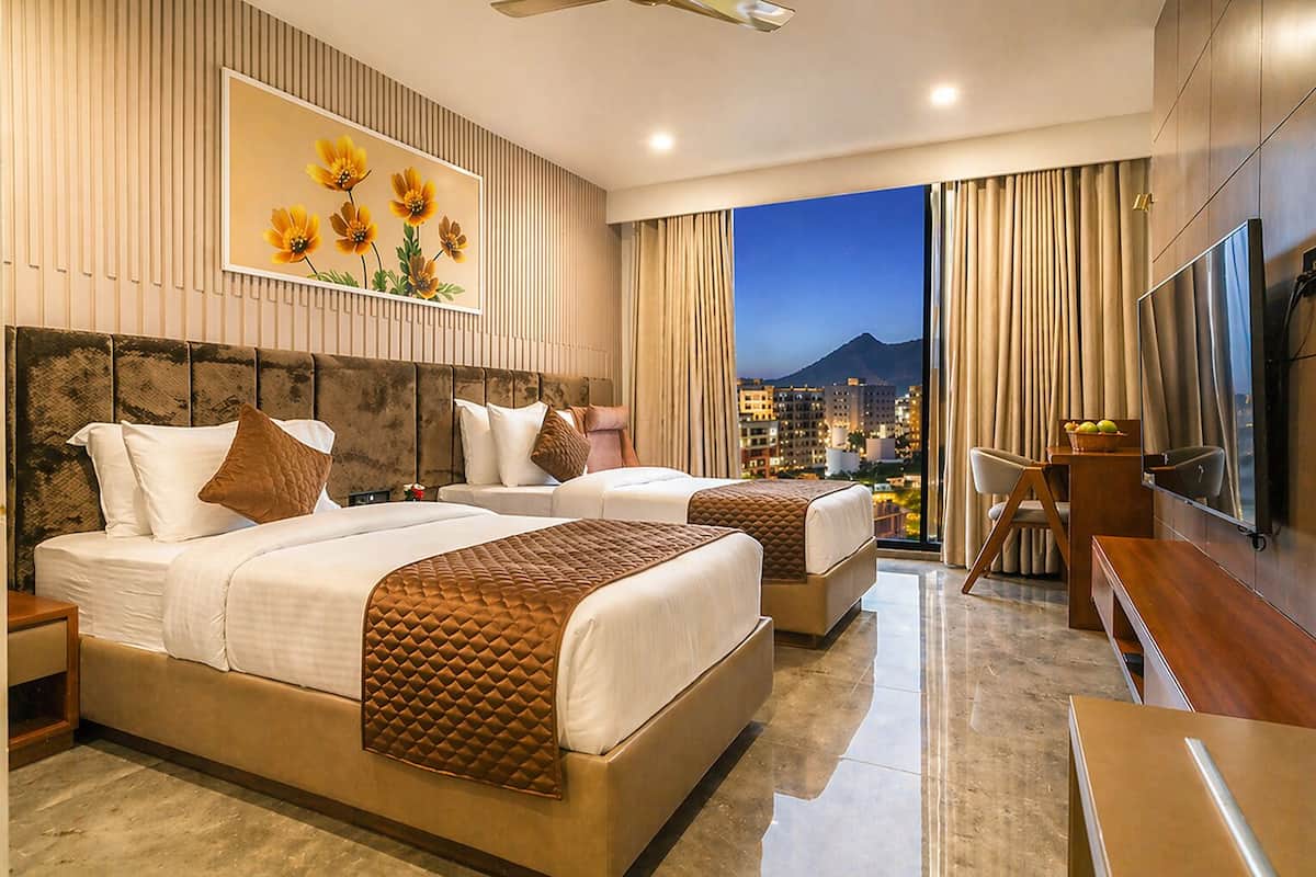 A hotel room with two beds, a TV, a desk, and a city view.