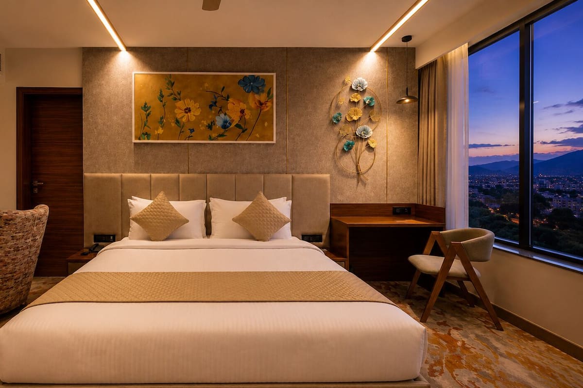 A modern hotel room with a large bed, a nightstand, a chair, a desk, and a large window with a city view.